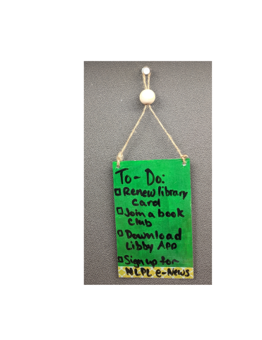 Green doorhanger with a string hanging from a push pin. Text reads " To-Do: Renew Library Card, Join a Book Club, Download Libby App, Sign up for NLPL e-News"